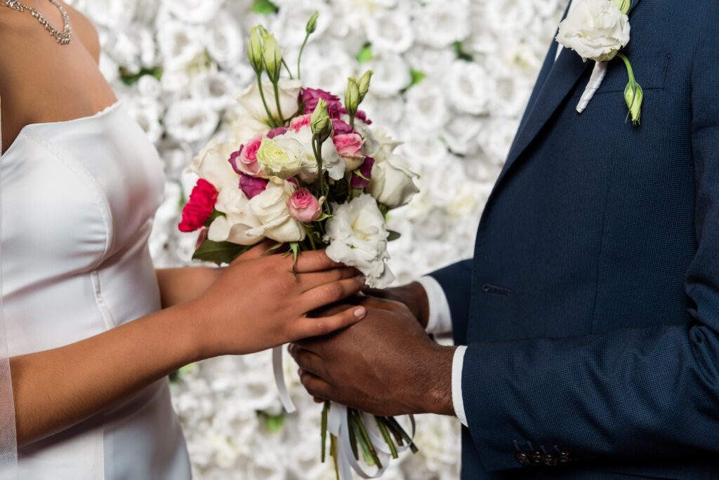 cropped view of african american bridegroom and bride holding flowers